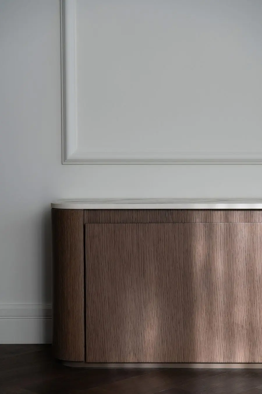 Curved walnut cabinet under a moulded wall panel