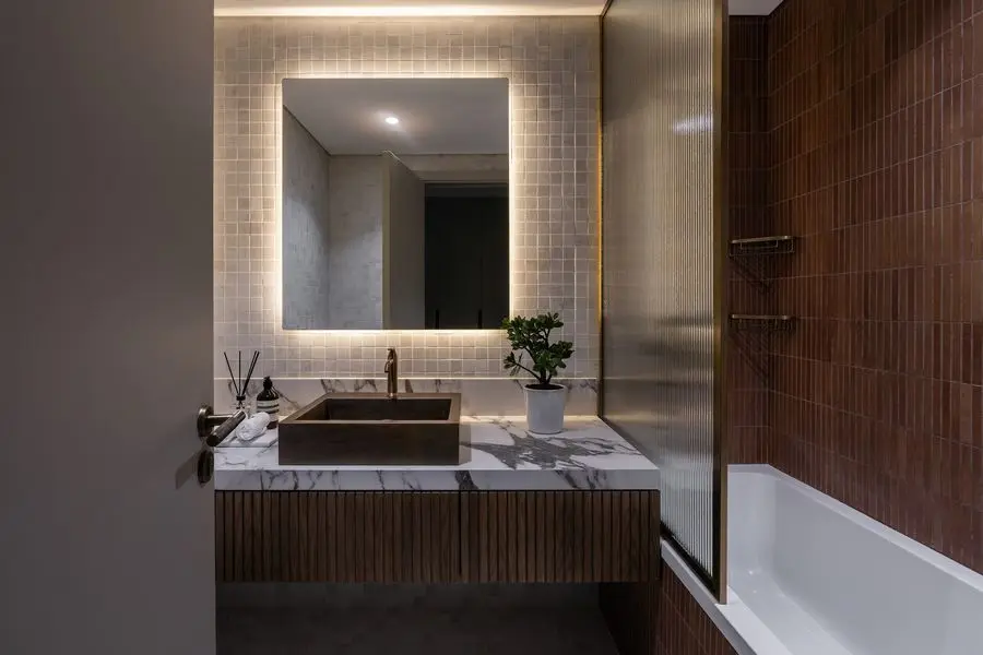 Bathroom with copper-toned tile, a backlit mirror and a floating vanity