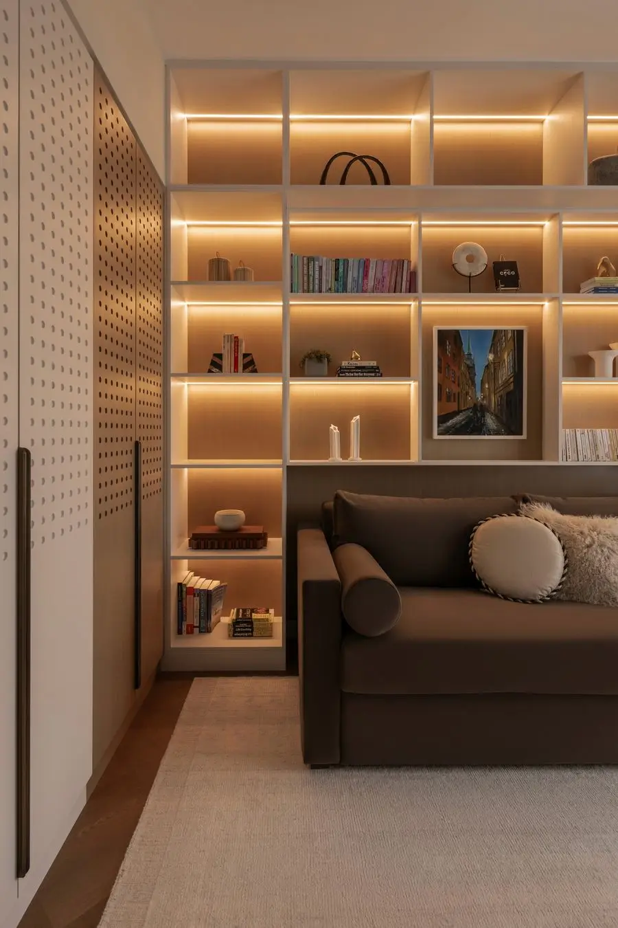 Backlit built-in shelving wall behind a brown sofa