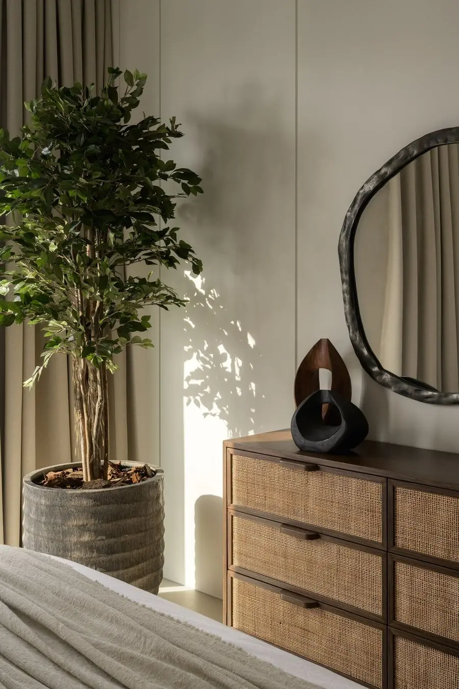 Bedroom corner with a rattan chest and a sculptural mirror