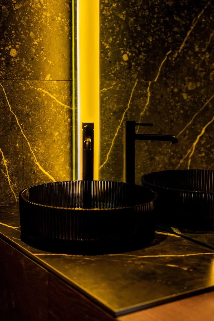 Black vessel basin on gold-veined stone with backlighting