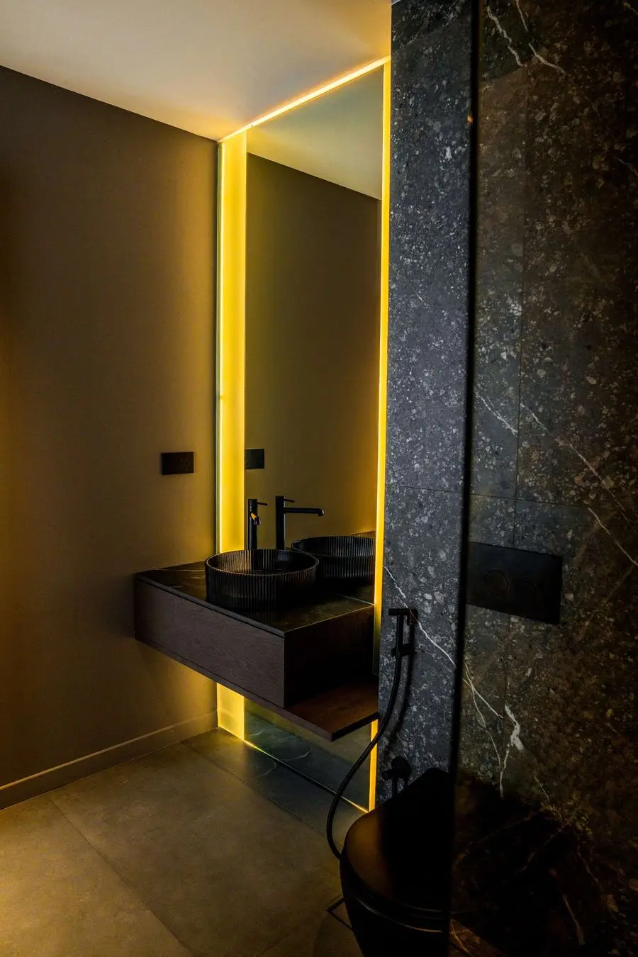 Backlit mirror above a black basin and gold-veined stone