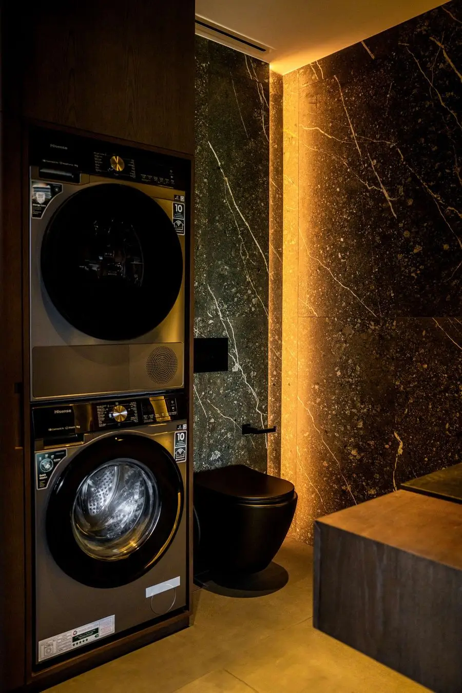 Stacked laundry machines beside a backlit stone wall