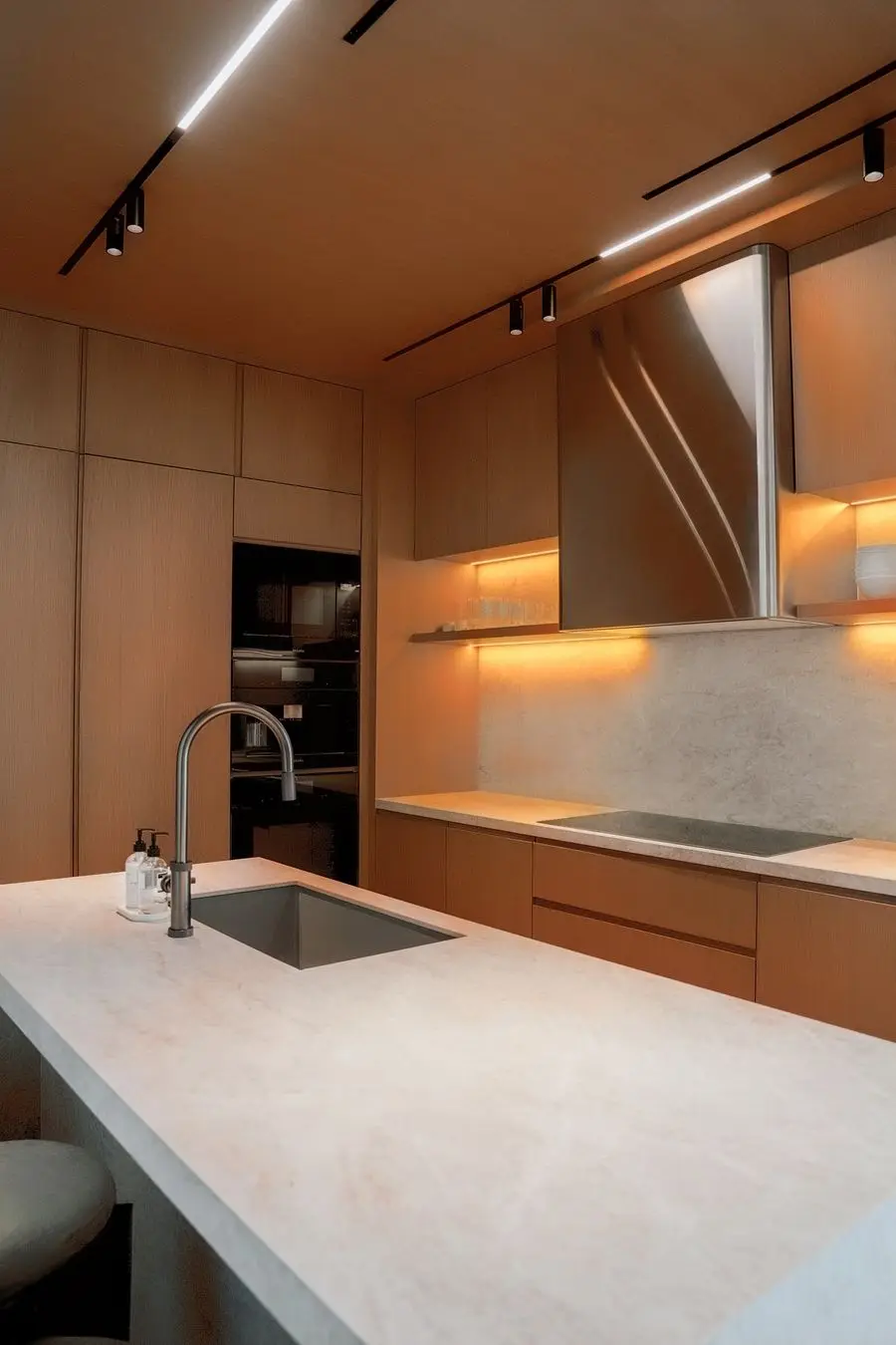 Light oak kitchen with a pale stone island and warm under-cabinet light