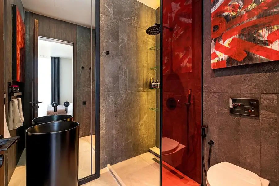 Bathroom with a black vessel basin, grey stone and a red glass shower screen