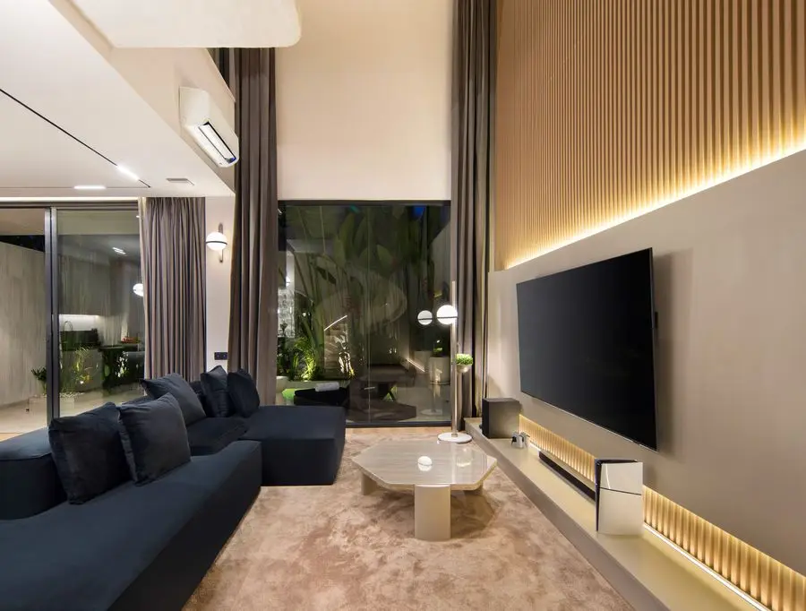Double-height living room with backlit timber slats and a charcoal sectional