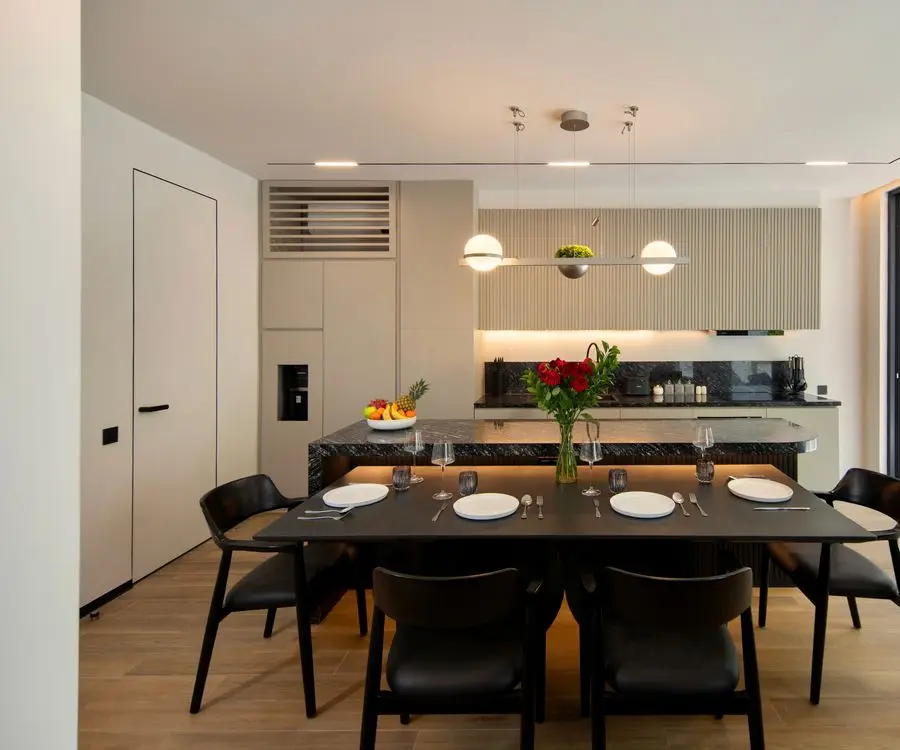 Dining table with black chairs in front of a white kitchen with a stone island