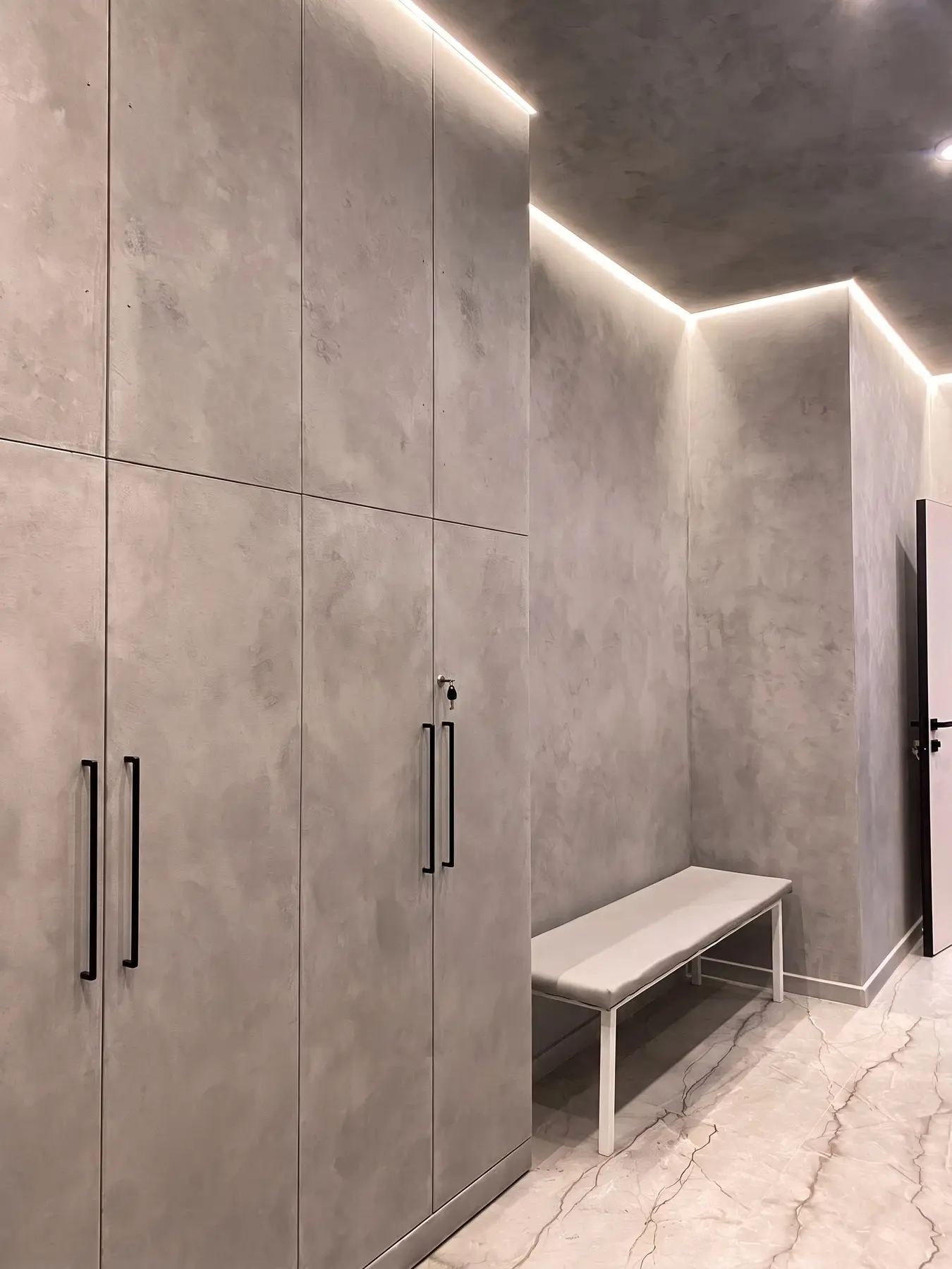 Foto real: pasillo terminado por nuestros maestros en estuco mineral gris efecto concreto, con iluminación LED perimetral